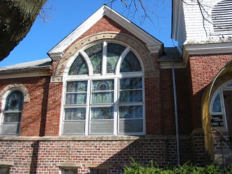 red brick church with beautiful large stained glass window and a bit of white frame belfry