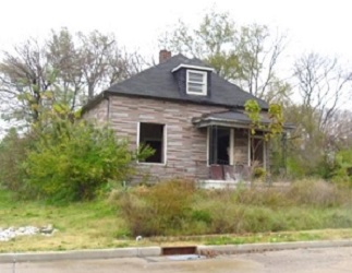 house with windows out and overgrown vegetation