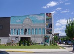 large mural on side of building with some landscaping and other art on the vacant lot in front of it