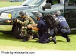 armed swat team crouching behind vehicle