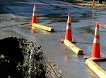 small sinkhole in street with orange traffic cones around it