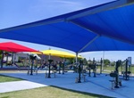 shade sails in primary colors are mounted over a fitness area along a greenway