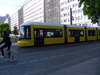 Attractive Transit and Active Transportation in Dense Neighborhoods Gives a Reason to Move Toward the City Center yellow tram, bicyclist, and attractive pedestrian environment in Berlin